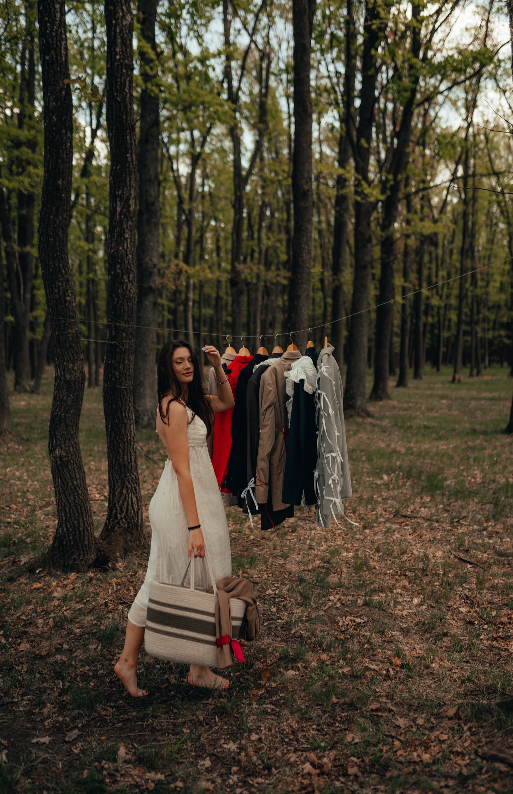 Gabi Denisa in a white dress, beside the re.born rail hung between trees in the forest