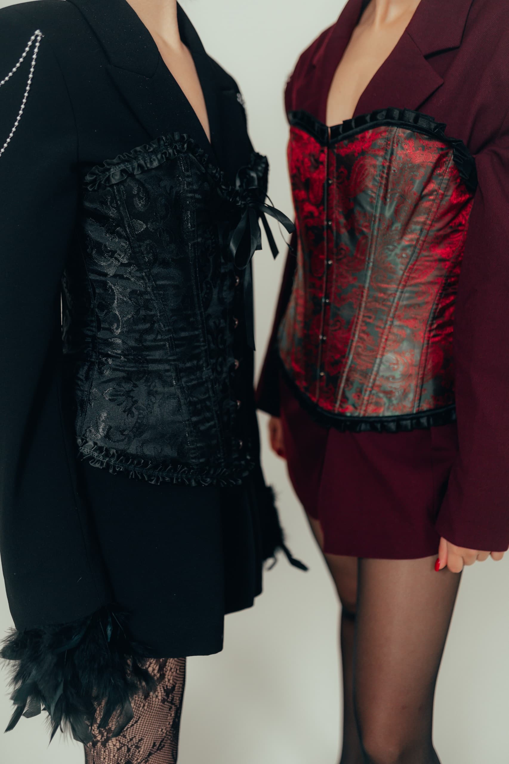 Two looks side by side, brocade corsets laced over oversized blazers in black and burgundy