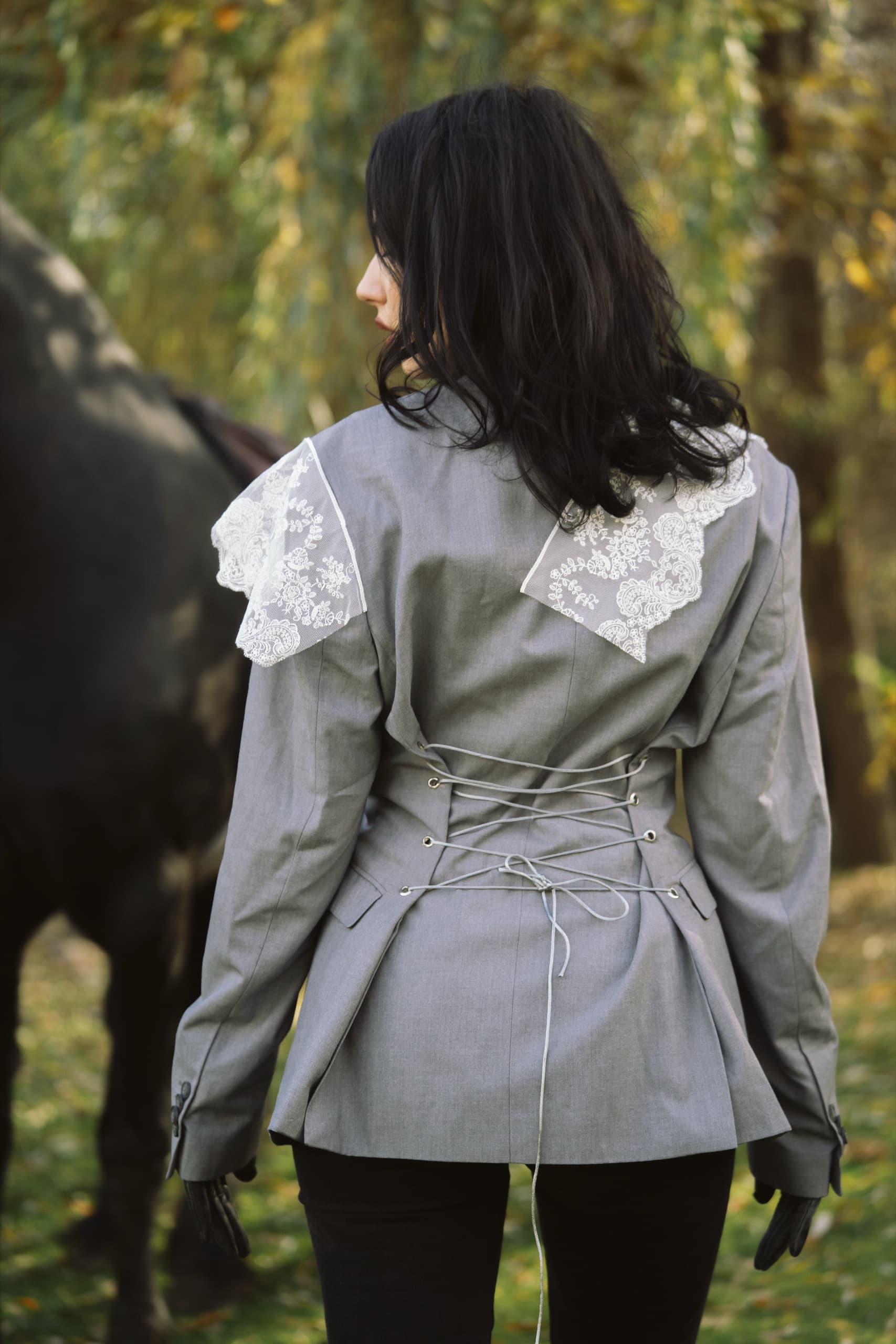 Back view of a grey blazer with corset lacing and white lace draped over the shoulders