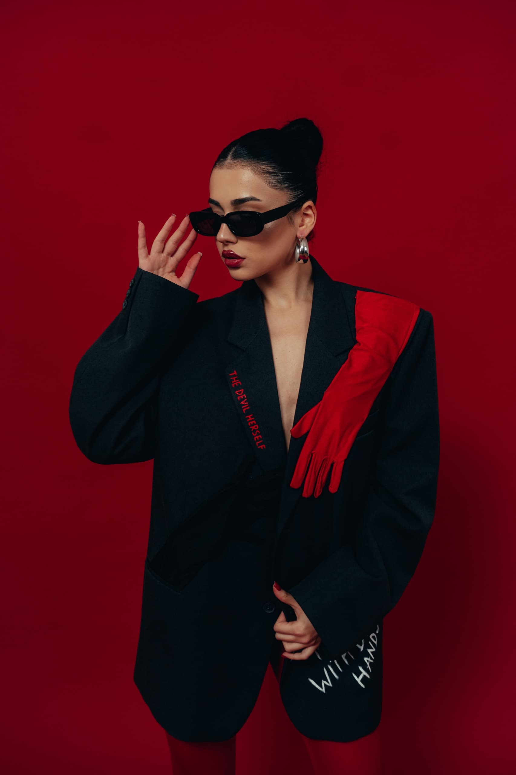Charcoal blazer with a red glove applique and embroidered lapel, against a deep red backdrop