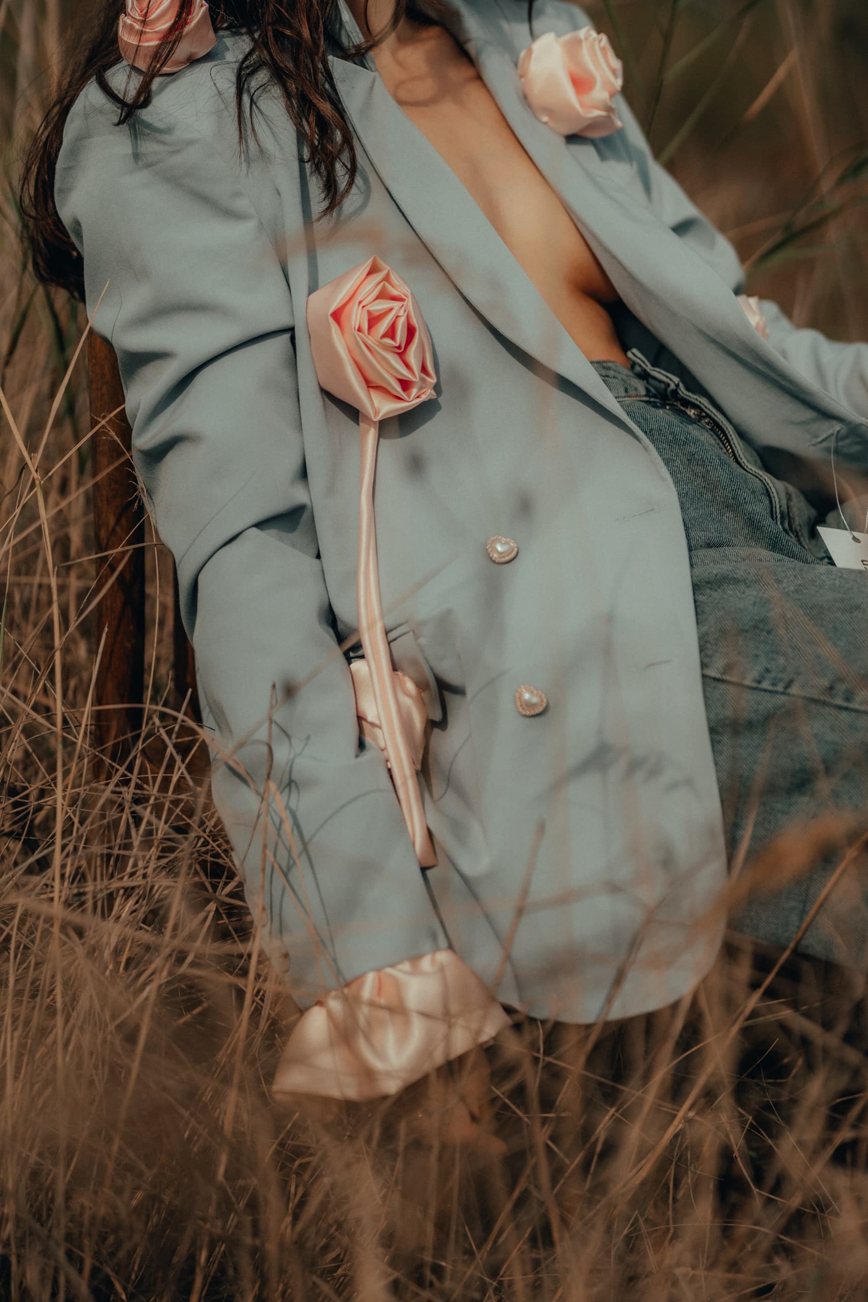 Dusty blue blazer with pink satin rose appliques and pearl heart buttons, seated in tall dry grass