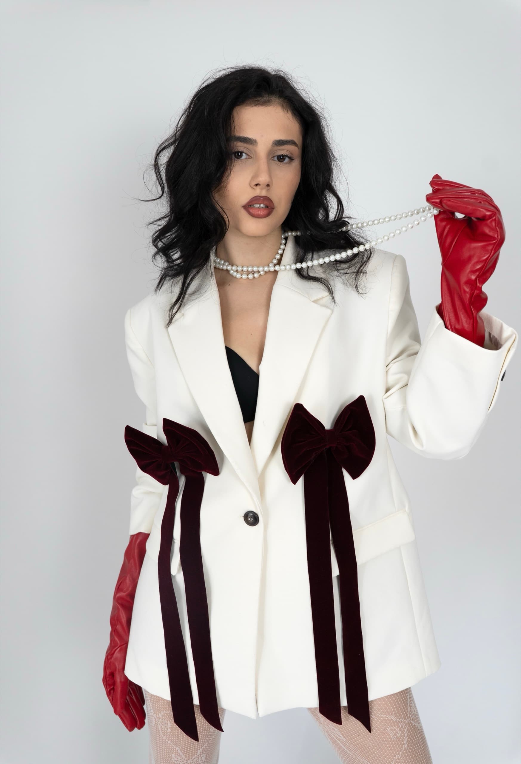 Cream blazer with burgundy velvet bows and trailing ribbons, styled with long leather gloves and pearls