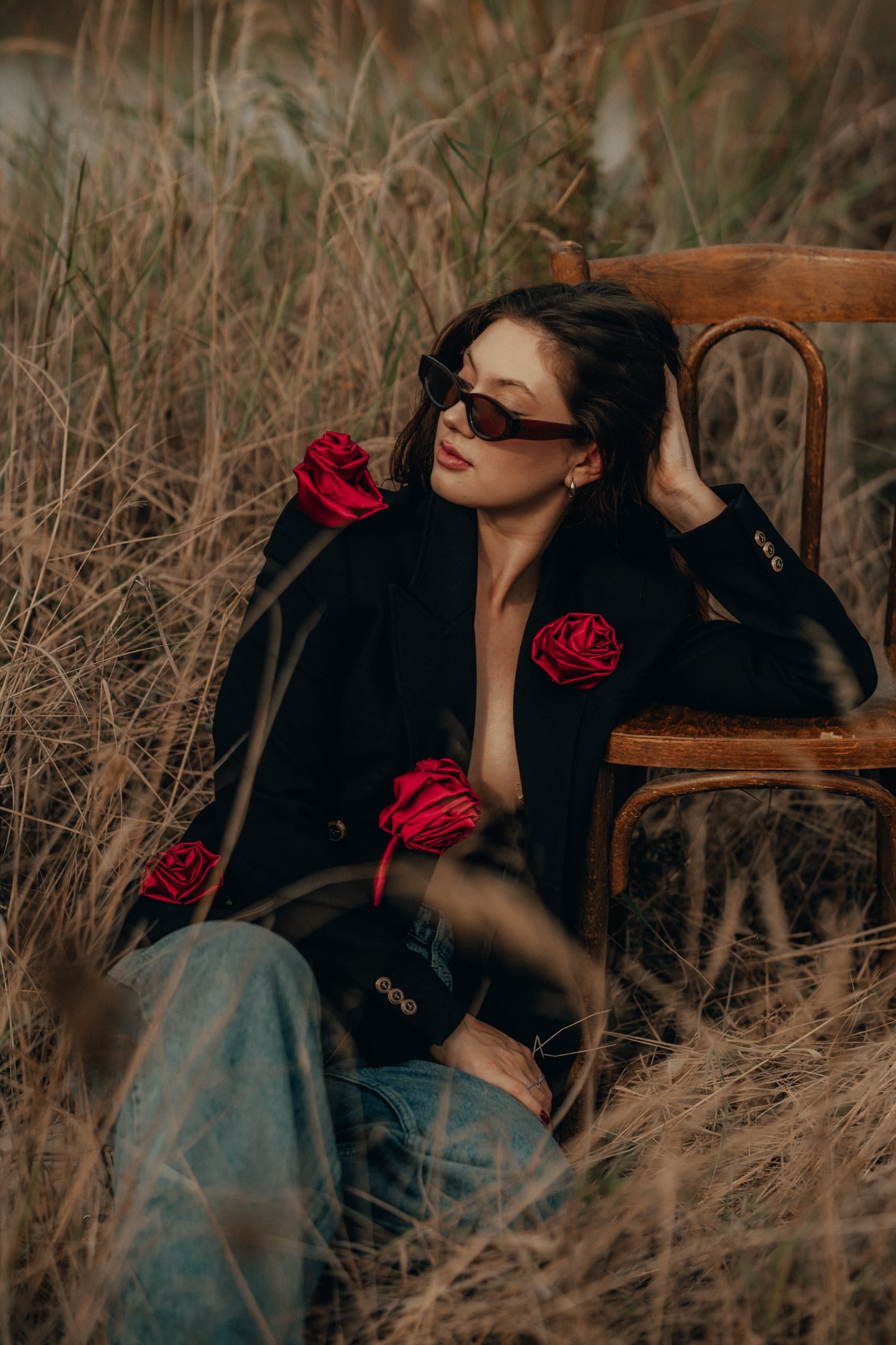 A black blazer trimmed with red fabric roses, on a wooden chair in dry grass