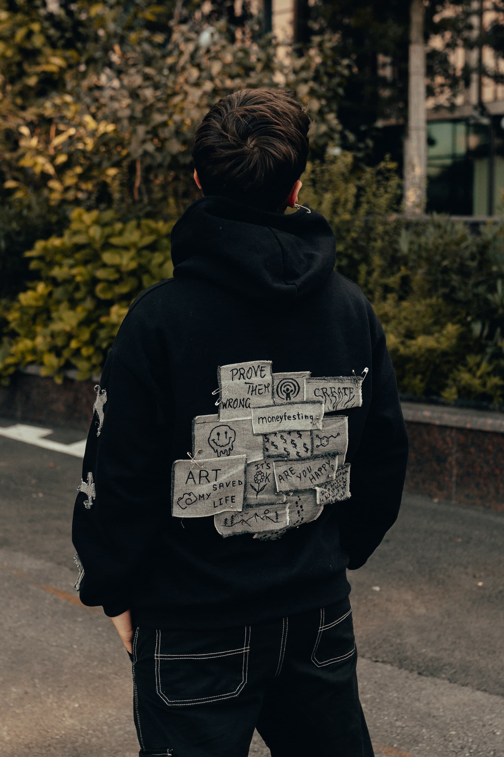 Back of a black hoodie covered in hand-lettered fabric patches reading prove them wrong, create and art