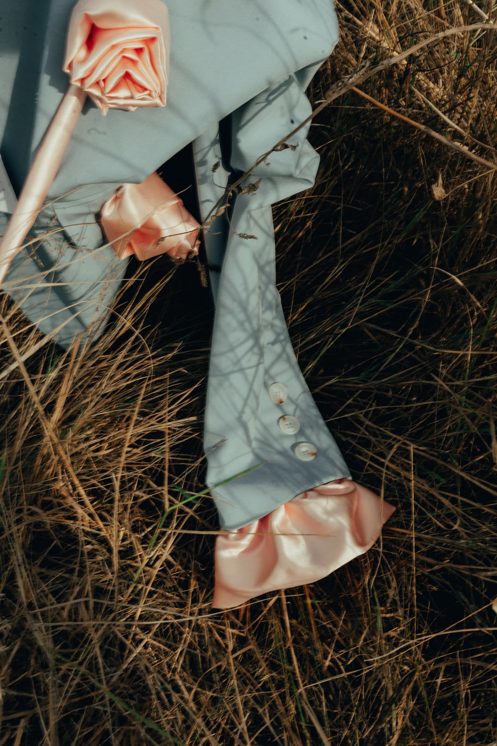 A pale mint garment with gathered peach satin ruffle cuffs, laid out in dry grass