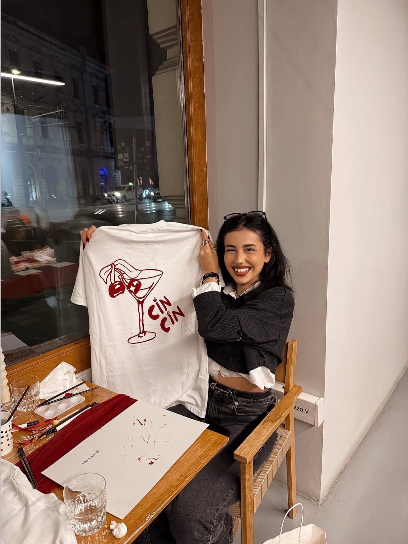 Someone holding up a tee they hand-painted with a cherry cocktail and the words cin cin